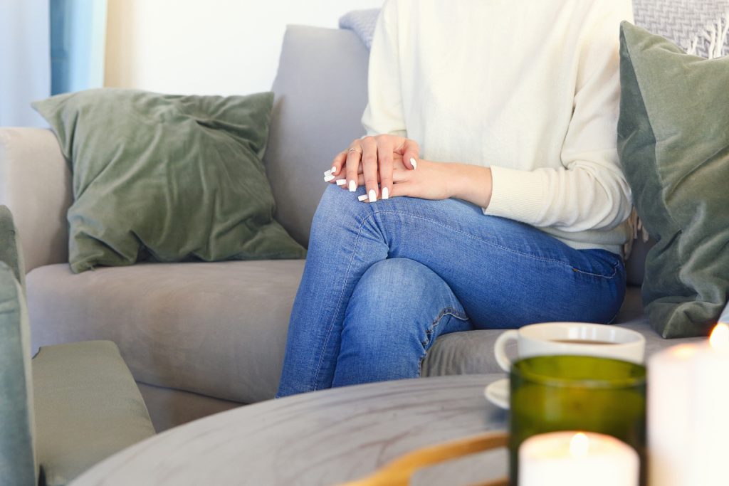 A woman sitting on a couch with folded hands, symbolizing reflection and emotional support during difficult parenting moments. | navigating relationships with adult children​